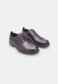 Chaussures habillées en cuir marron avec un bout arrondi, un laçage et des détails de couture subtils. Présentent une semelle contrastante et une tirette au talon.