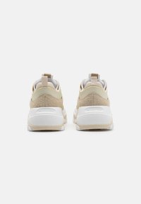 Beige og hvite sneakers med teksturert overdel, polstret ankelkrage og en robust gummisåle med merking på hælen.