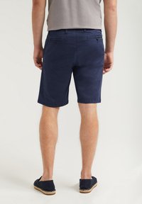 Marina bomullsshorts med rak framkant, två bakfickor och sömmar vid fållarna, tillsammans med svarta espadrillos på bara fötter.