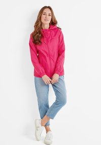 Lightweight, pink rain jacket with a full front zipper, elastic cuffs, and adjustable hood. Worn over light blue jeans and white sneakers.