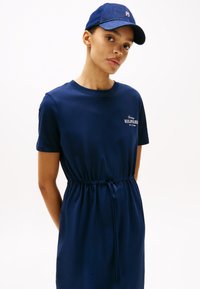 Robe en coton bleu marine à manches courtes, avec taille à cordon et logo Tommy Hilfiger. Associée à une casquette bleu marine assortie.
