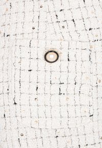 Tifă albă din tweed cu fire negre și aurii, având un model texturat, un buzunar frontal și un buton decorativ din perlă.