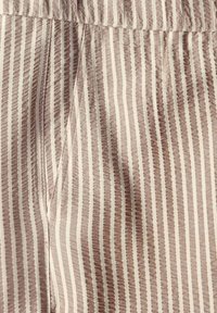 Nära bild av beige och vit vertikalt randig tyg med en sidoficka och söm för midjebandet.