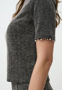 Top grigio a maniche corte con motivo houndstooth e finitura testurizzata, caratterizzato da accenti di perle e strass sui polsini e un design cropped.