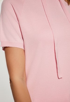 Top in maglia rosa a maniche corte con vestibilità rilassata, scollo a V con dettaglio a fiocco e texture liscia. Tessuto leggero con una sottile lucentezza.