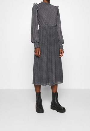 Vestido midi de patrón en blanco y negro con mangas largas abullonadas y detalles con volantes en los hombros, combinado con botas negras de plataforma con cordones.