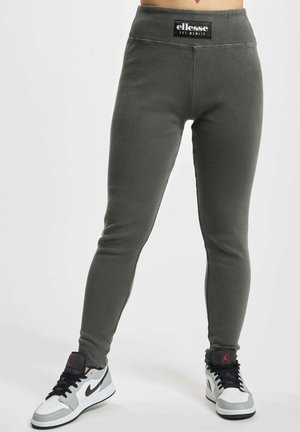 Ciemnoszare prążkowane legginsy z naszywką z logo ellesse na talii, noszone z białymi, szarymi i czarnymi sneakersami Nike Air Jordan.