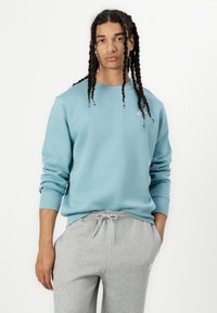 Φωτεινό γαλάζιο βαμβακερό φούτερ με στρογγυλή λαιμόκοψη και ριμπ μανσέτες, συνδυασμένο με γκρι φόρμες με ελαστική μέση με κορδόνι και πλαϊνές τσέπες.