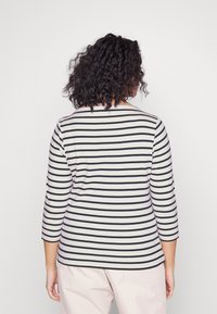Sort og hvid stribet bluse med lange ærmer, bådudskæring og 3/4-ærmer, lavet af et blødt og glat materiale. Enkel design, tætsiddende form.