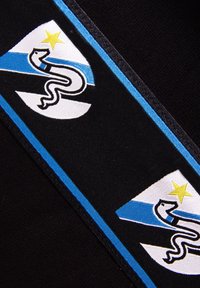 Zwarte stof met twee geborduurde logo's in een blauw-witte design, met een slang en een gele ster op een schildvorm.