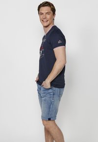 Námořnické tričko s krátkým rukávem a bílým a červeným proužkovaným límcem, na přední straně s grafickým designem. Spárováno s ohrnutými světle modrými denimovými šortkami.