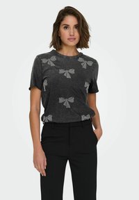 Camiseta negra de manga corta con un diseño metálico texturizado de lazos. La tela parece suave y casual, complementando unos pantalones negros.