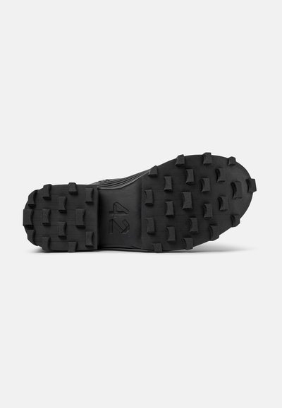 Suola di scarpa in gomma nera con lugs multidirezionali e una sezione centrale rialzata, caratterizzata da un logo prominente e una superficie texture per migliorare la trazione.