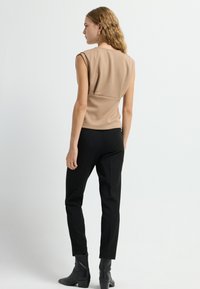 Beige mouwloos topje met ronde halslijn, gestructureerde stof en getailleerd ontwerp. Gecombineerd met zwarte op maat gemaakte broeken en enkelboots.