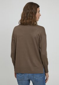 Pull en tricot marron à coupe décontractée, col rond et accents côtelés. Les fentes latérales augmentent le confort ; associé avec un jean bleu.