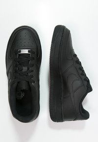 Černé kožené tenisky s texturovaným povrchem, polstrovaným límcem a gumovou podrážkou. Obsahují perforovanou špičku, šněrování a malé kovové logo.