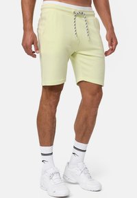 Lysegule bomulds shorts med elastisk talje, snor og sidelommer. Båret med hvide sneakers og stribede sokker.