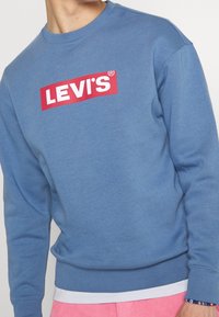 Felpa blu in misto cotone con polsini e orlo a coste. Presenta un logo LEVI'S rosso ben visibile sul petto.