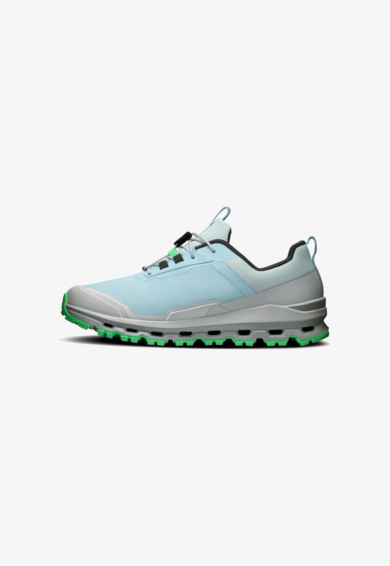 Chaussure de sport basse bleu clair avec semelle grise et bande de roulement verte, avec lacets noirs et gris et boucles de traction au talon et à la languette.