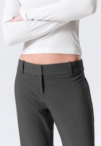 Pantalon gris sur mesure avec une texture lisse, présentant une coupe ajustée et un design avant plat subtil, complété par des passants pour ceinture.