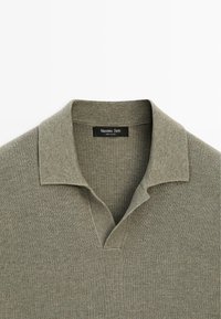 Olivgrünes gestricktes Poloshirt mit umgeklapptem Kragen und V-förmigem Ausschnitt, Etikett trägt die Aufschrift „Massimo Dutti, Made in China.“