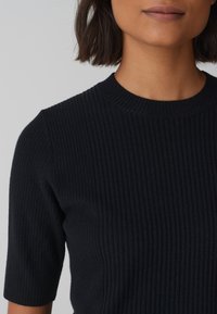 Zwarte ribgebreide top met een ronde halslijn en korte mouwen. De textuur heeft verticale strepen voor een gestructureerde uitstraling.