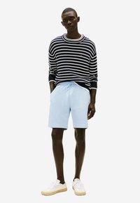 Pull rayé navy avec un col rond, short bleu clair et baskets blanches. Les matériaux semblent être en coton ; le design est décontracté et ajusté.