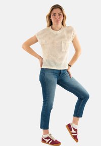 Ivory kortemouwen gebreide top met een gestructureerd patroon, gecombineerd met blauwe slim-fit jeans en kastanjebruine sneakers met witte strepen.