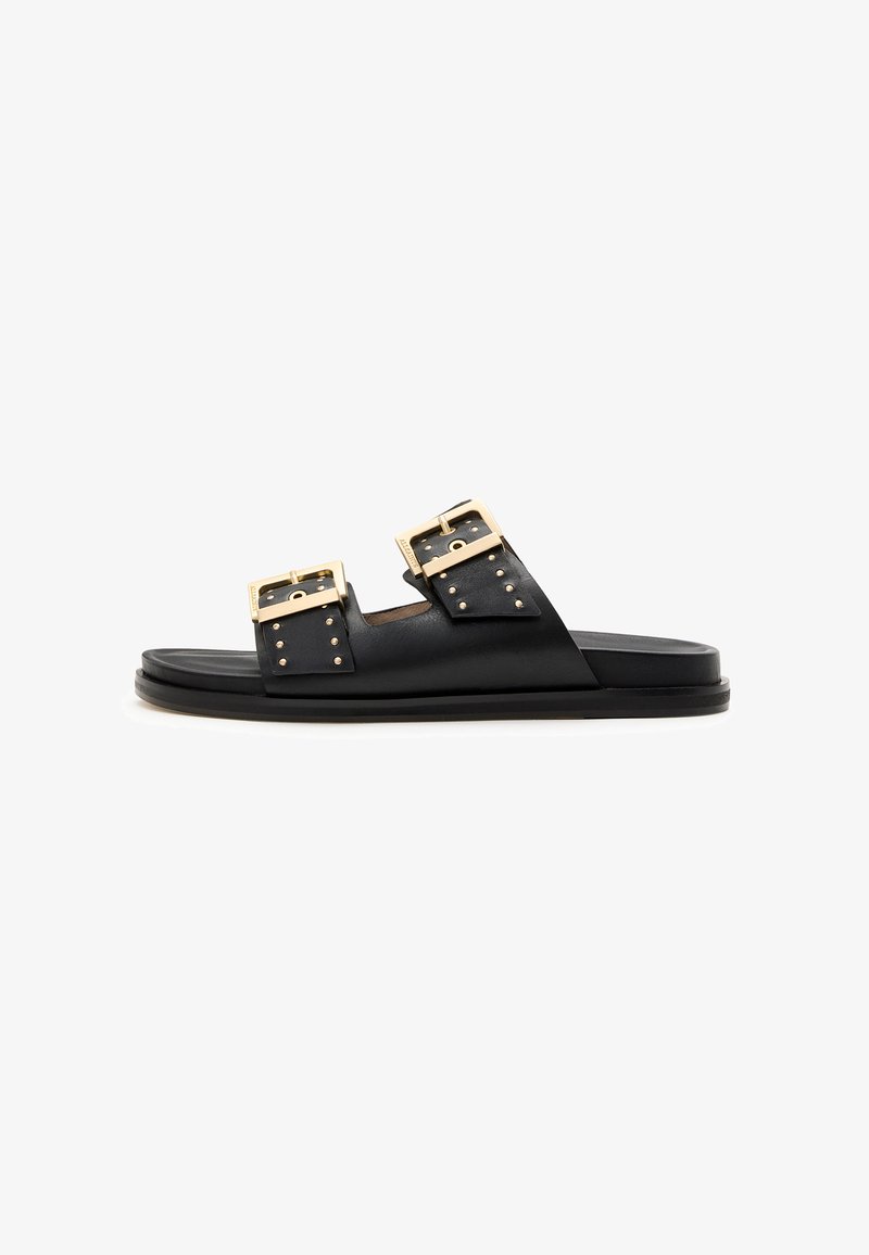 Black leather slide sandal featuring two large gold buckles and studded accents. Flat sole with a minimalist design and smooth texture.