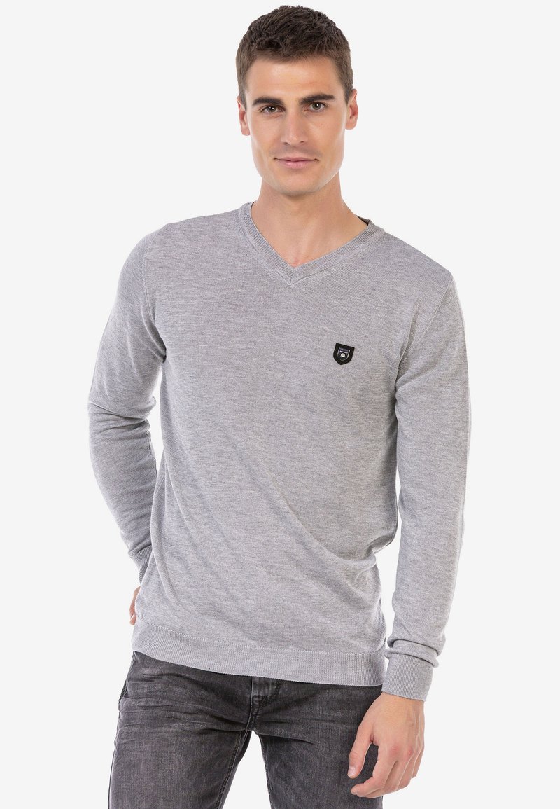 Grauer V-Ausschnitt-Pullover aus Strickstoff mit langen Ärmeln und gerippten Bündchen, ausgestattet mit einem kleinen schwarzen Logopatch auf der oberen linken Seite.