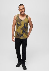 Trøye med et abstrakt camouflasjemønster i olivengrønn, gul og marineblå. Kombinert med svarte jeans og støvler.