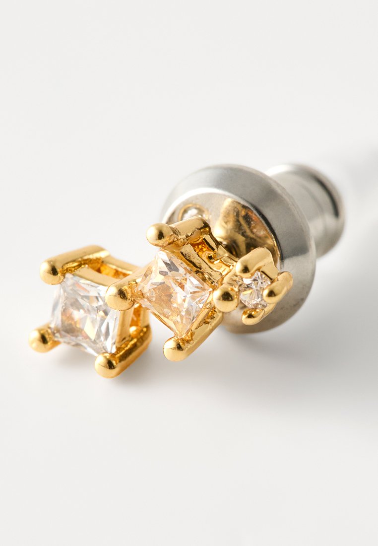 Ohrringe in Goldfarbe mit zwei quadratisch geschliffenen Kunstdiamanten, einer größer und einer kleiner, die in Krappenfassungen gesetzt sind. Metallrückseite mit glatter Oberfläche.