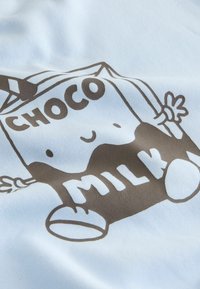 Svijetloplava tkanina s crtežem u stilu crtanog filma na kojem je prikazana kutija čokoladnog mlijeka s rukama, koja se smiješi, uz natpis "CHOCO MILK" u tamnosmeđoj boji.