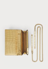 Zlata vilka s teksturovanym vzorom krokodíla, so zipsovým priehradkom a zlatými reťazovými popruhmi. Hladký kožený interiér s lesklým povrchom.