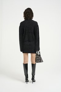 Svart teksturert genser med cropped design, kombinert med et matchende skjørt. Tilbehør inkluderer en mønstret håndveske og høyglans knee-high støvler.