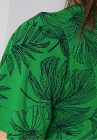 Zelené bavlněné tričko s velkými námořnickými květinovými vzory, krátkými rukávy a volným střihem. Hladká textura s podrobnými potisky.