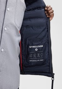 Lichtgrijze buitenlaag zip-up jack met een marineblauwe gevoerde binnenkant. Bevat een zak met verzorgingsinstructies en logo op de voering.