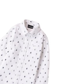 Camicia bianca con bottoni, caratterizzata da un motivo nautico di ancore blu e velieri. Colletto chiuso con una tasca sul petto. Tessuto dalla texture liscia.