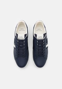 Sneaker blu navy con tomaia in pelle liscia, dettagli in strisce bianche, punta rotonda e lacci piatti. Logo visibile sulla linguetta.