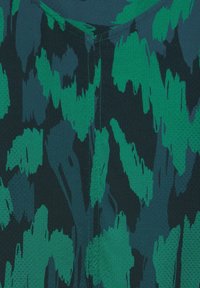 Ciemnozielony materiał tekstylny z wzorem, który zawiera jasne zielone plamy i łatki, chropowata powierzchnia oraz kontrastowe detale szwów.