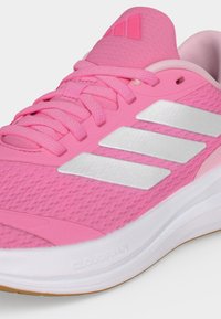 Chaussure de course rose avec les trois bandes blanches Adidas, lacets roses, col rembourré et semelle blanche affichant le texte « Cloudfoam ».