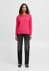 Pull fuchsia à encolure large et manches longues, associé à un jean droit gris foncé et des ballerines noires.