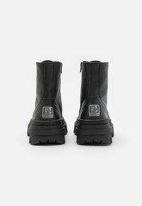 Paire de bottines en cuir noir avec semelles épaisses et écussons du logo Steve Madden à l'arrière, vues de dos sur fond blanc.