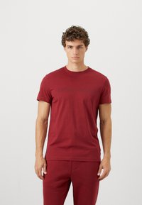 Tricou din bumbac roșu cu mâneci scurte, având un logo negru embosat "BJÖRN BORG" pe piept. Textură netedă, croială clasică.