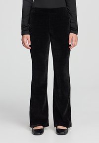 Pantaloni svasati in velluto corduroy nero con un ampio cinturino in vita, texture liscia, aderenti attraverso le cosce e che si allargano verso l'orlo.