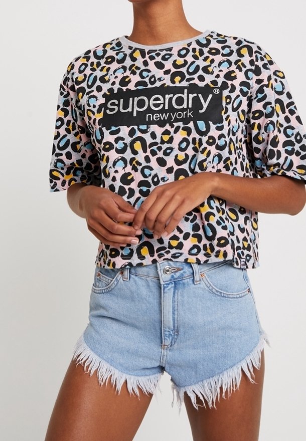 Osoba oblečená v leopardím vzoru Superdry New York crop topu a světle modrých roztrhaných denimových šortkách, stojící se zkříženýma rukama.
