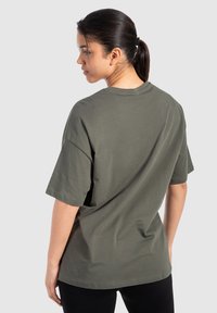 Camiseta de algodón verde oliva con mangas cortas y cuello redondo; corte relajado, con costuras visibles en el dobladillo y el escote.