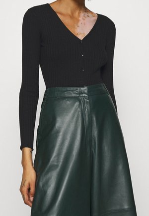 Top noir à manches longues à côtes avec un col en V et des boutons à l'avant, associé à une jupe en cuir vert foncé à taille haute et texture lisse.