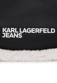 Melna ādas soma ar balta mākslīgā pūkaina apdari, uz priekšu izceltas teksta "KARL LAGERFELD JEANS" drukātām burtu lielajiem burtiem.