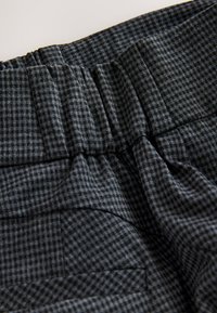 Tessuto a quadri grigio con vita elastica arricciata, caratterizzato da una texture sottile e un piccolo motivo a quadretti. Include un dettaglio con tasca laterale.